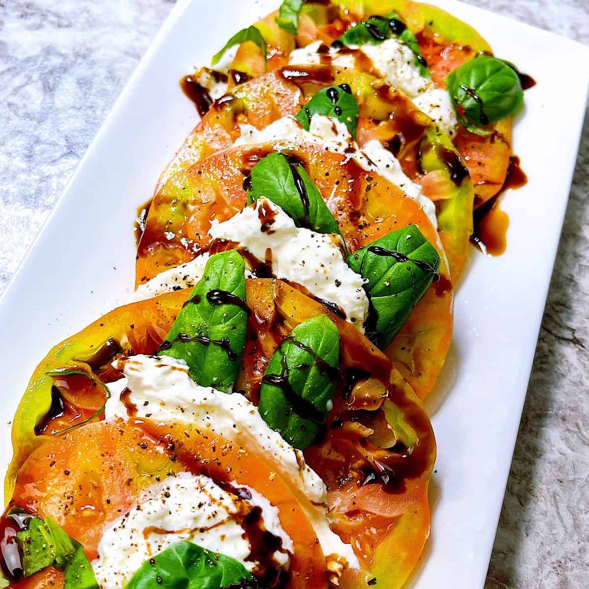 Heirloom Tomato Burrata Caprese on plate topped with basil and balsamic