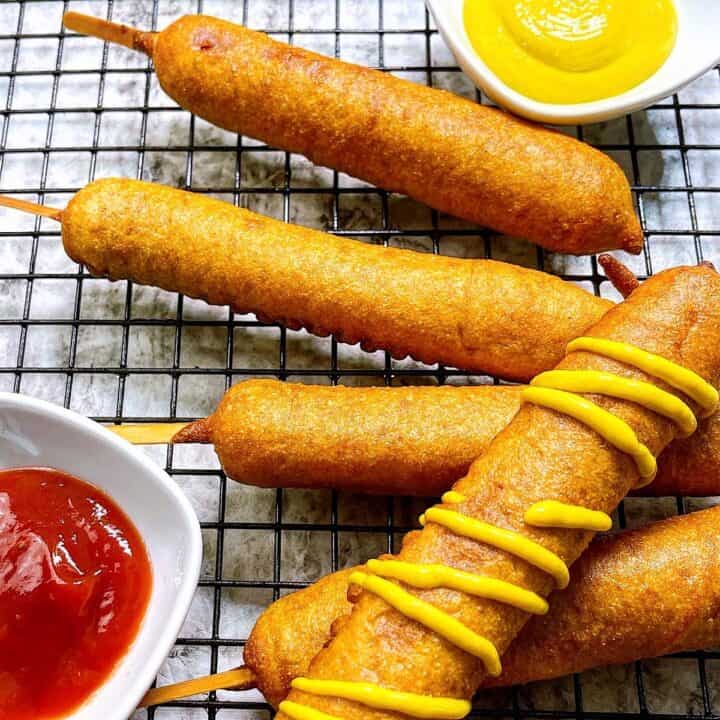 Honey Dipped Batter Corndogs on wire rack with mustard drizzle and ketchup for dipping