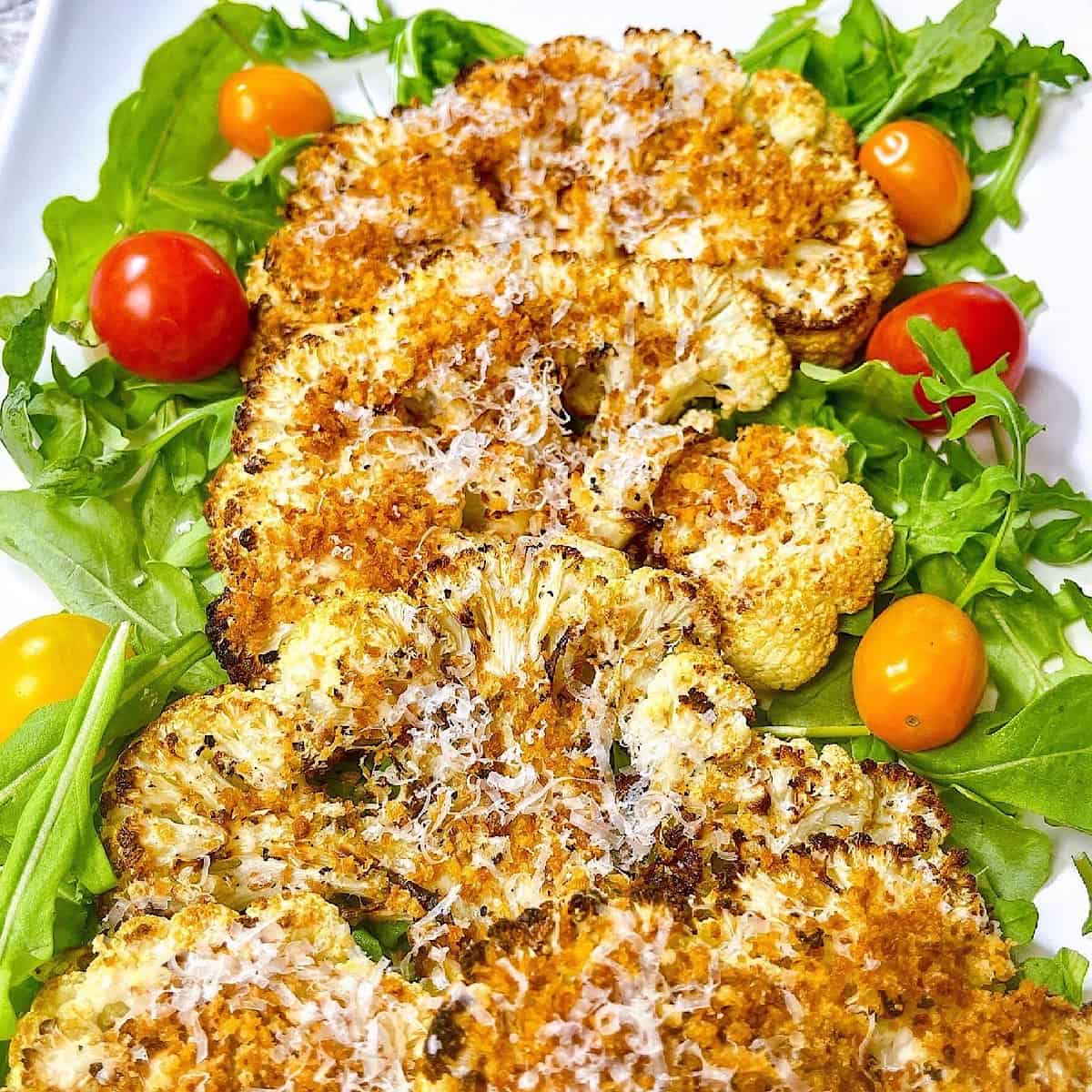 Panko and Parmesan Crusted Cauliflower Steaks on platter with arugula and tomatoes