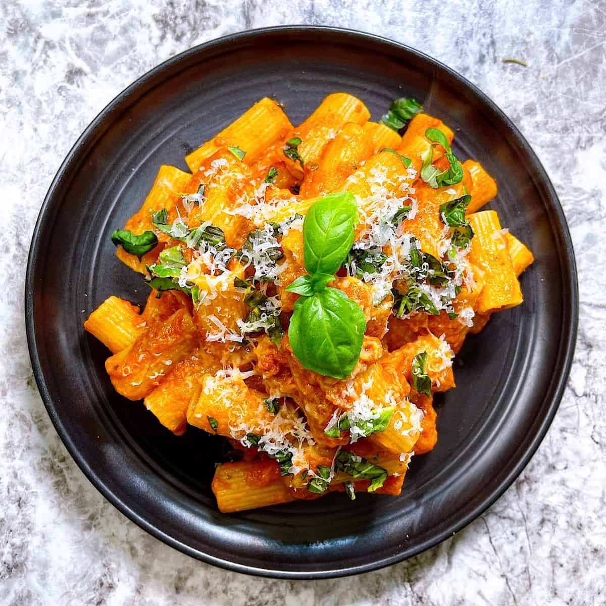 Pasta Alla Vodka on black plate topped with Parmesan and basil