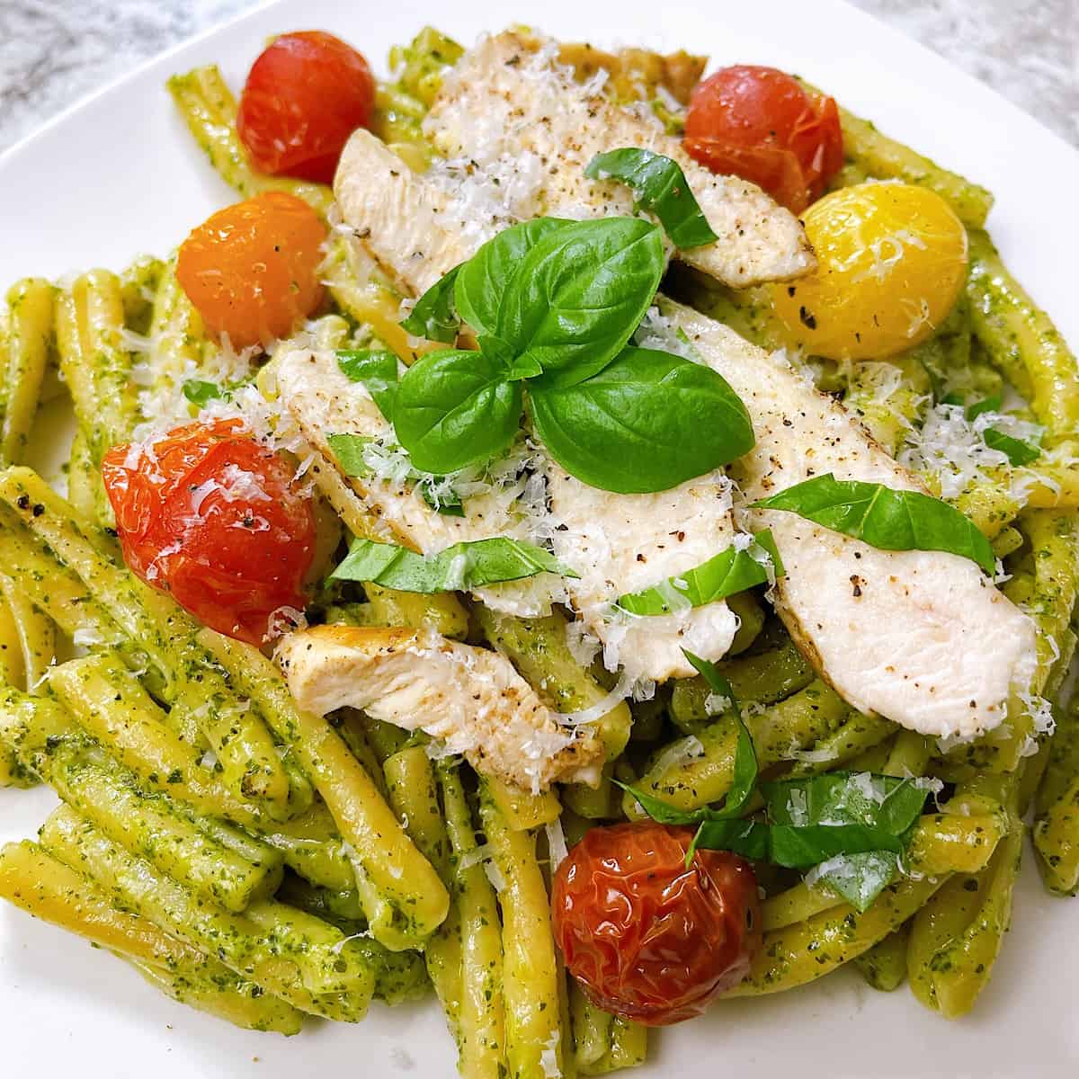 Pesto Casarecce with Chicken and Roasted Tomatoes in white bowl and topped with Parmesan and basil
