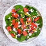 Watermelon salad in a white bowl showing all of the toppings.