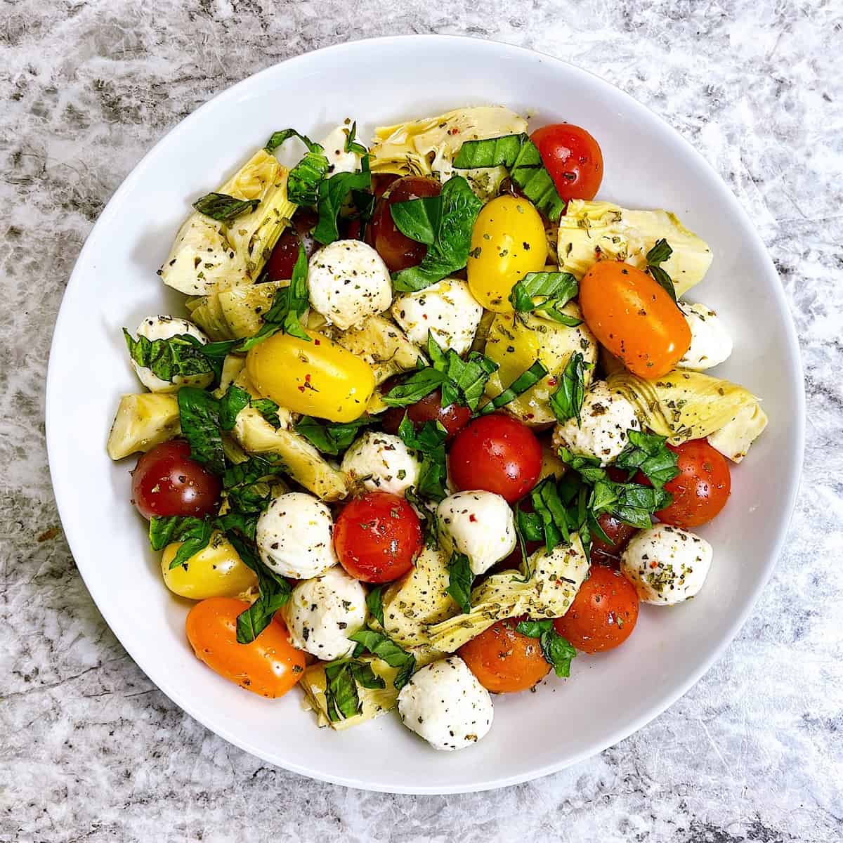 Tomato and Artichoke Caprese topped with red pepper and basil in white bowl