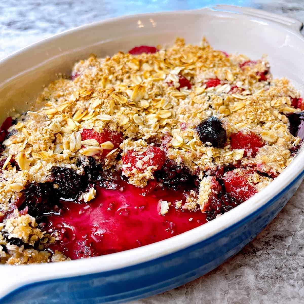 Triple Berry Crisp in ceramic crock with a large spoonful removed so you can see berries