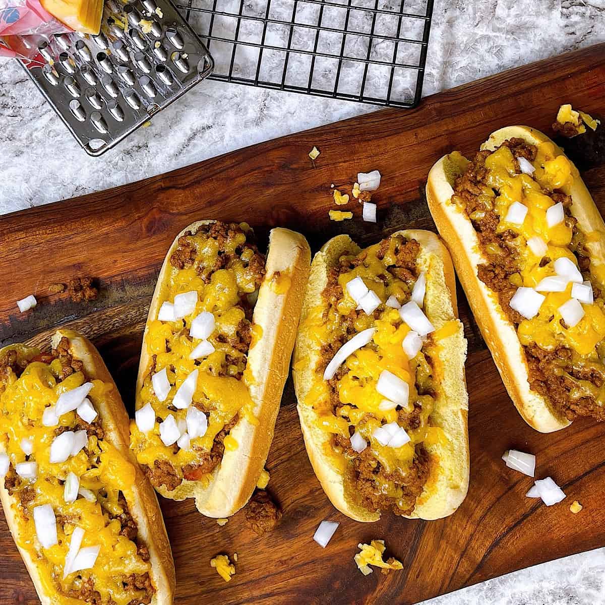 Air Fryer Chili Dogs on cutting board with shredded cheese and onion