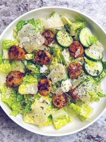 caesar salad with blackened scallops in white salad bowl