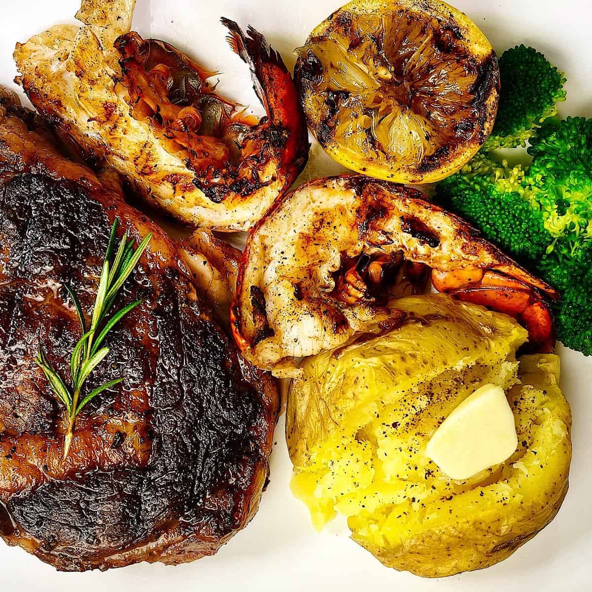 Surf and Turf​ on plate lobster steak potato and broccoli