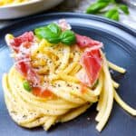 Pasta twirl of pasta alla carbonara on black plate topped with basil