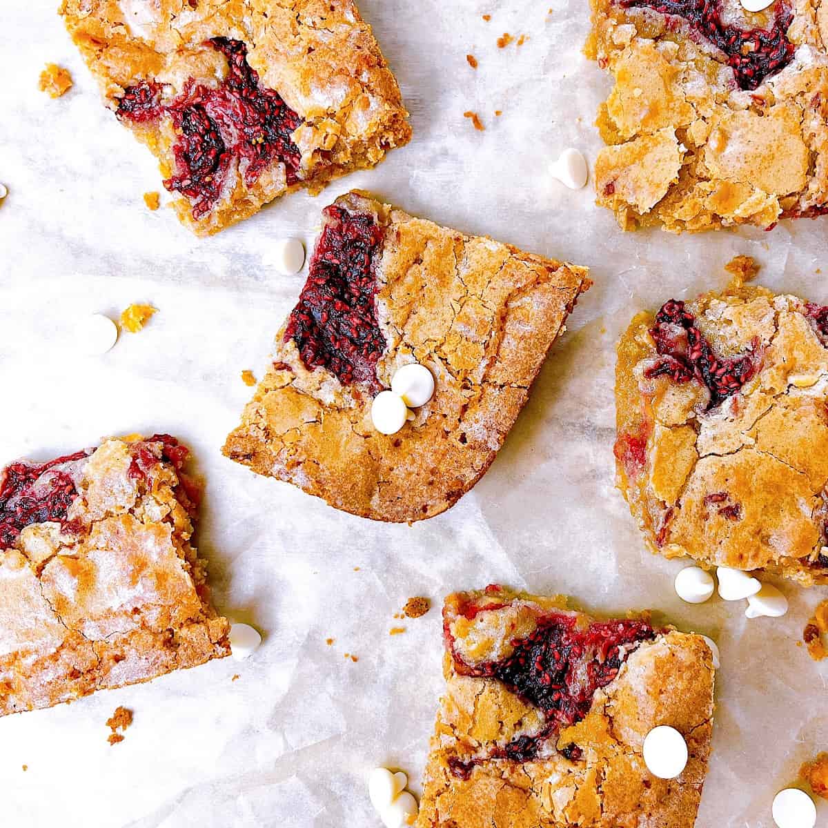 Raspberry and White Chocolate Blondies on parchment paper with white chocolate chips
