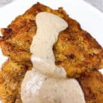 Chicken fried steak with white gravy on a white plate.