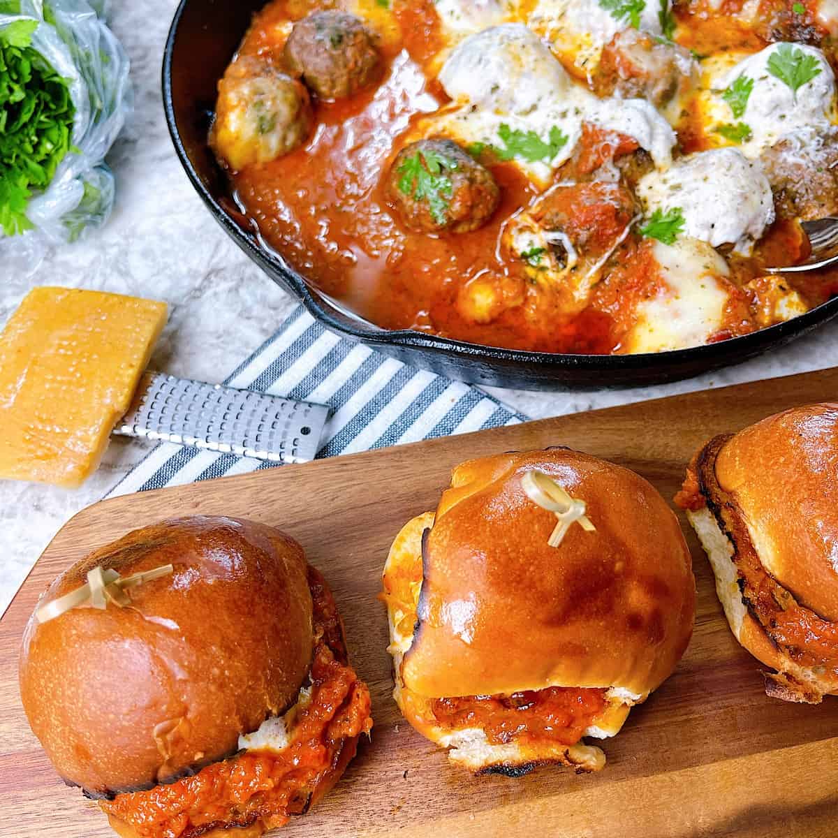 Meatball Sliders with melted cheese in skillet sitting next to sliders