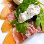 Prosciutto wrapped cantalope with burrata and arugula on a platter.