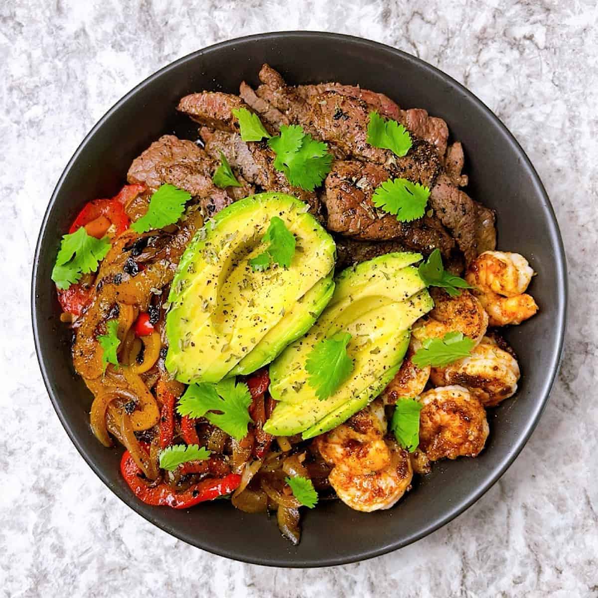 Steak and Shrimp Fajita Bowl topped with sliced avocado and cilantro