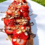 Sliced nutella toast with all the toppings on a plate outside in the sunlight.