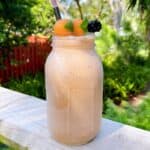 A melon banana smoothie sitting on the deck outside with garnish.