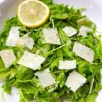 Arugula salad with lemon vinaigrette tossed in a white bowl.