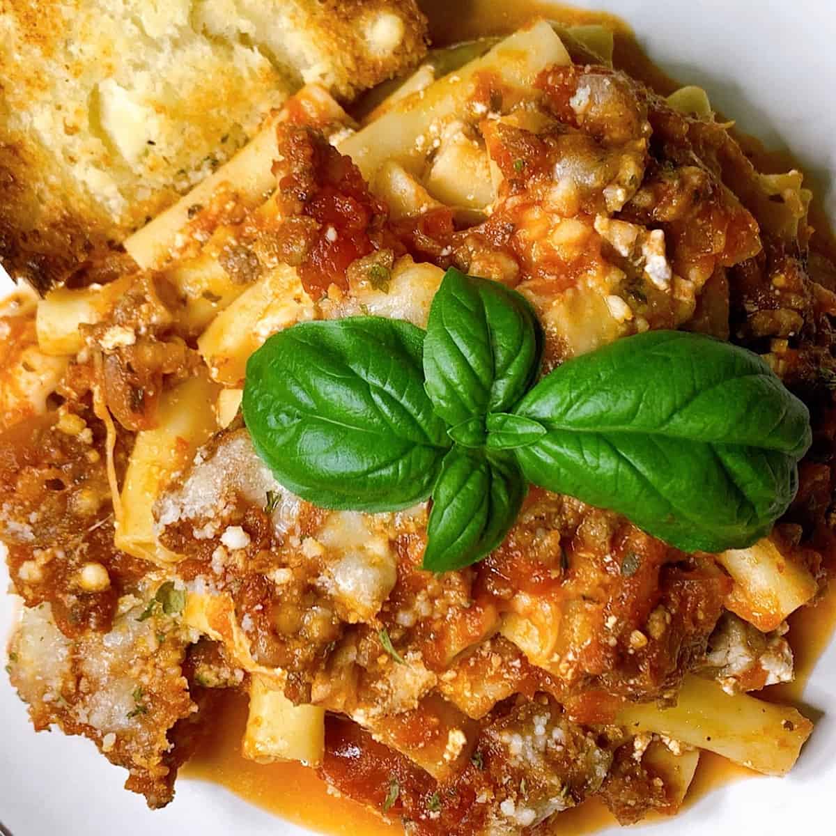 Baked ziti on a black plate topped with Parmesan and basil