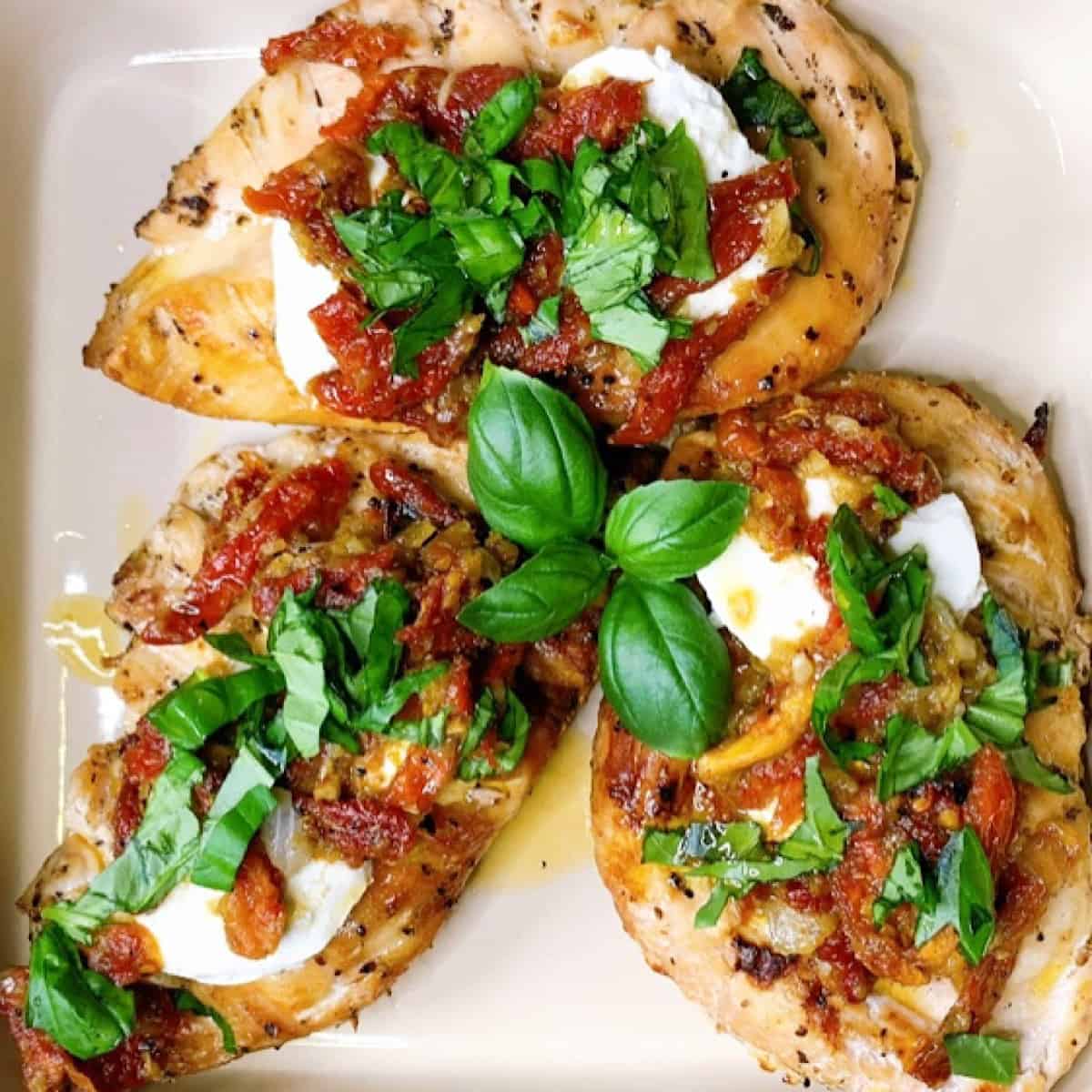 Chicken topped with goat cheese, sundried tomatoes, and chopped basil in a casserole dish.