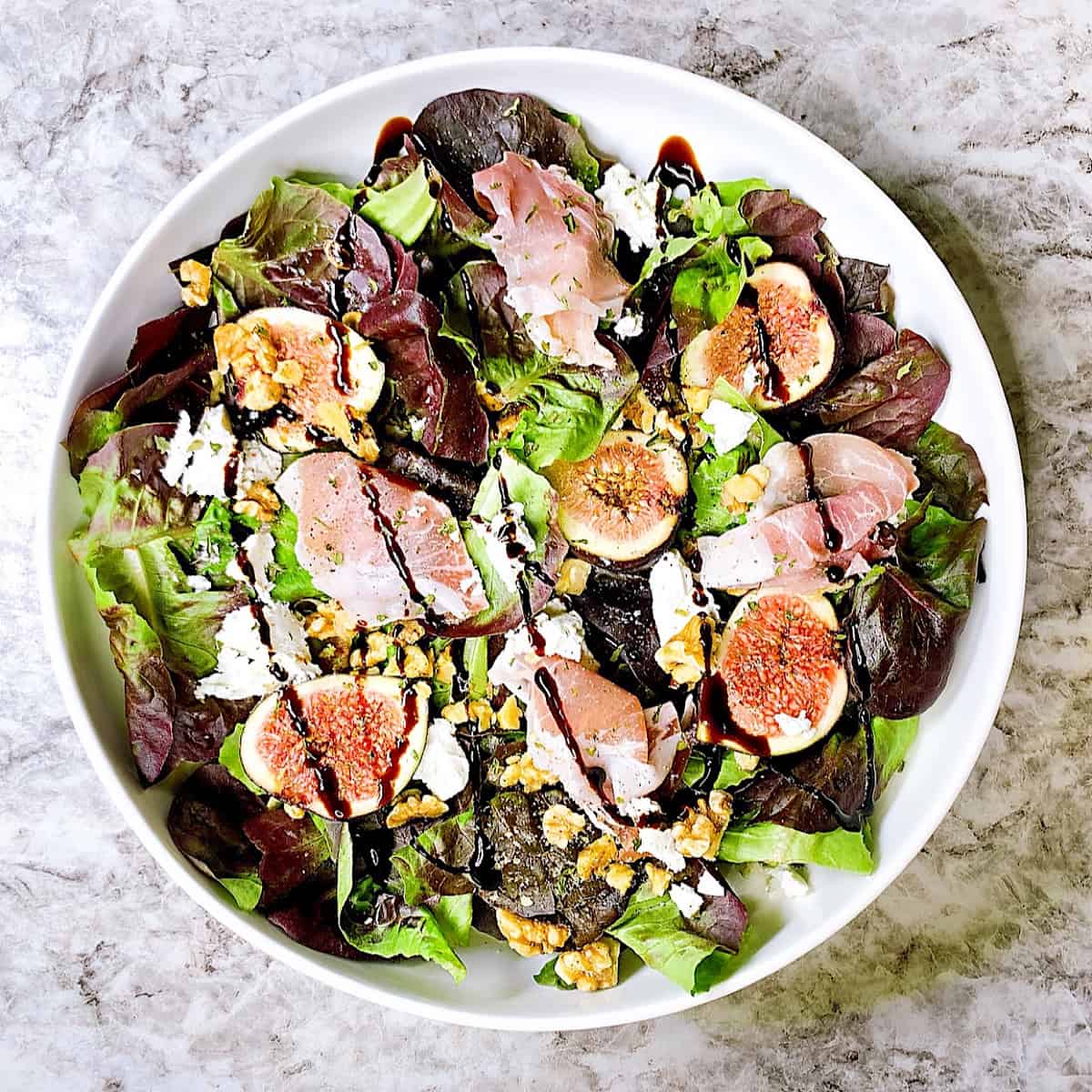 Fig and Prosciutto Salad in a large white bowl drizzled with balsamic glaze