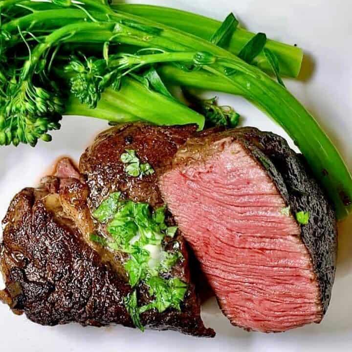 Filet Mignon sliced in half to show medium rare center and plated with broccolini.
