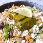 Greek orzo salad with dolmades in a black bowl with lemon garnish.