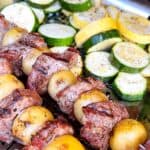 Lamb kabobs on metal skewers with a side of grilled zucchini and squash.