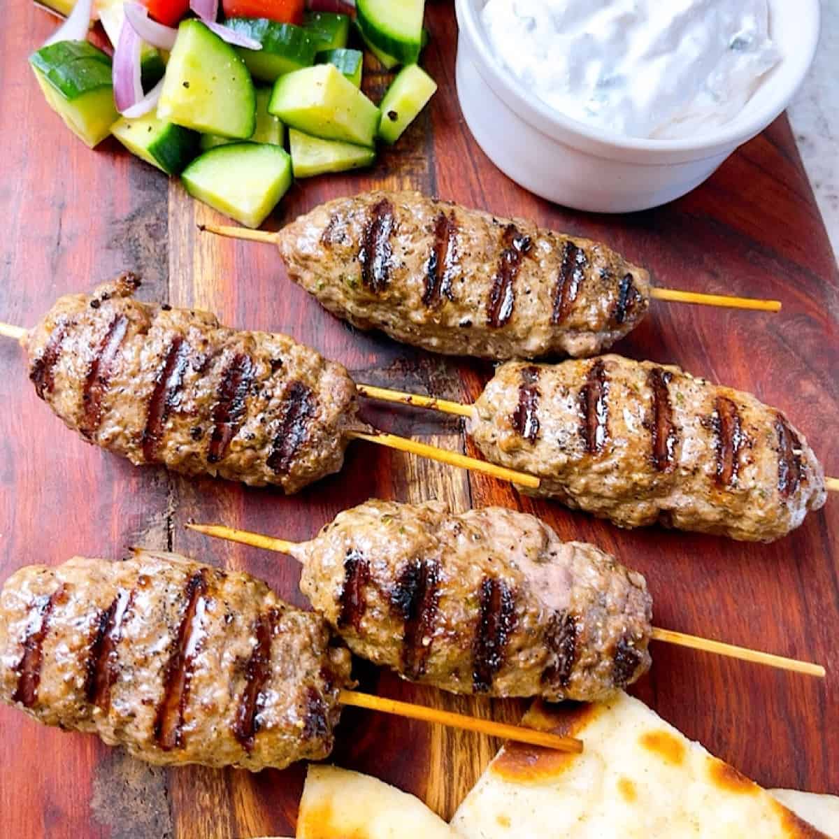 Lamb Kofta on stick with a side of tzatziki sauce pita bread tomatoes cucumber