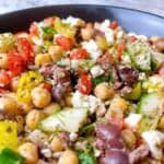 Mediterranean salad with chickpeas in a black bowl with dill and feta.