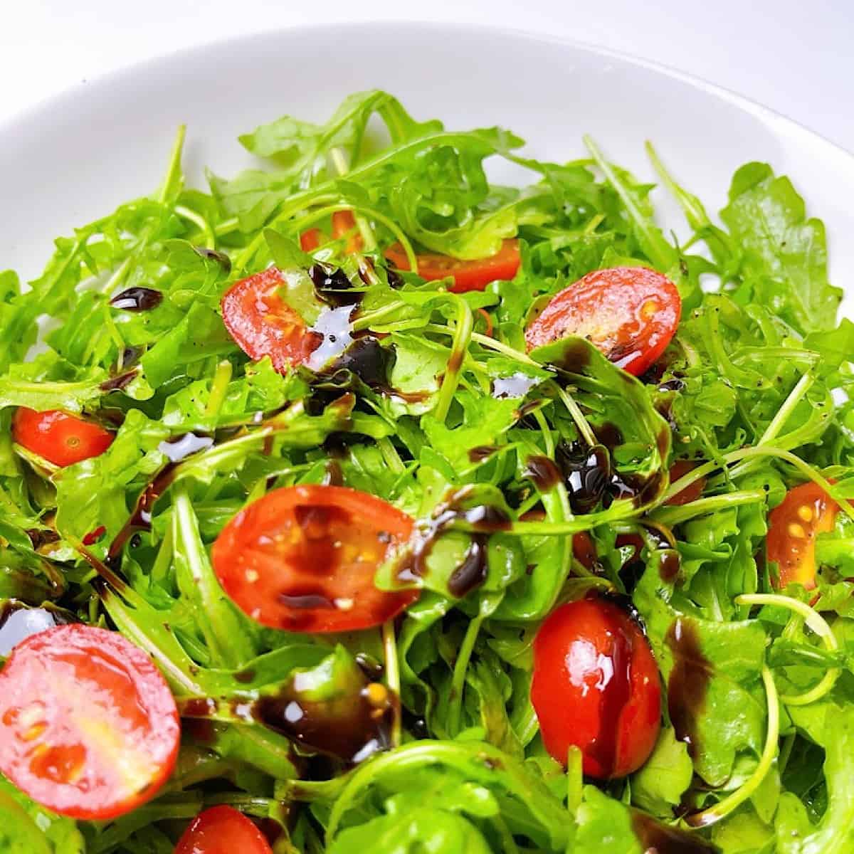 Close up of a arugula lettuce and cherry tomatoes with balsamic drizzle and salt and pepper