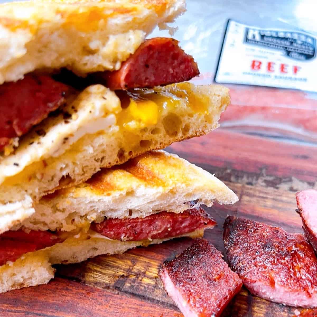 Smoked Sausage Breakfast Sandwich Open Faced and stacked with brand packaging in background