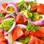 Tomato avocado salad tossed in a white bowl.