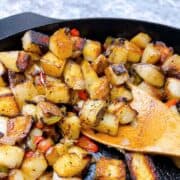 Cowboy Potatoes close up in cast iron skillet with wooden spoon.