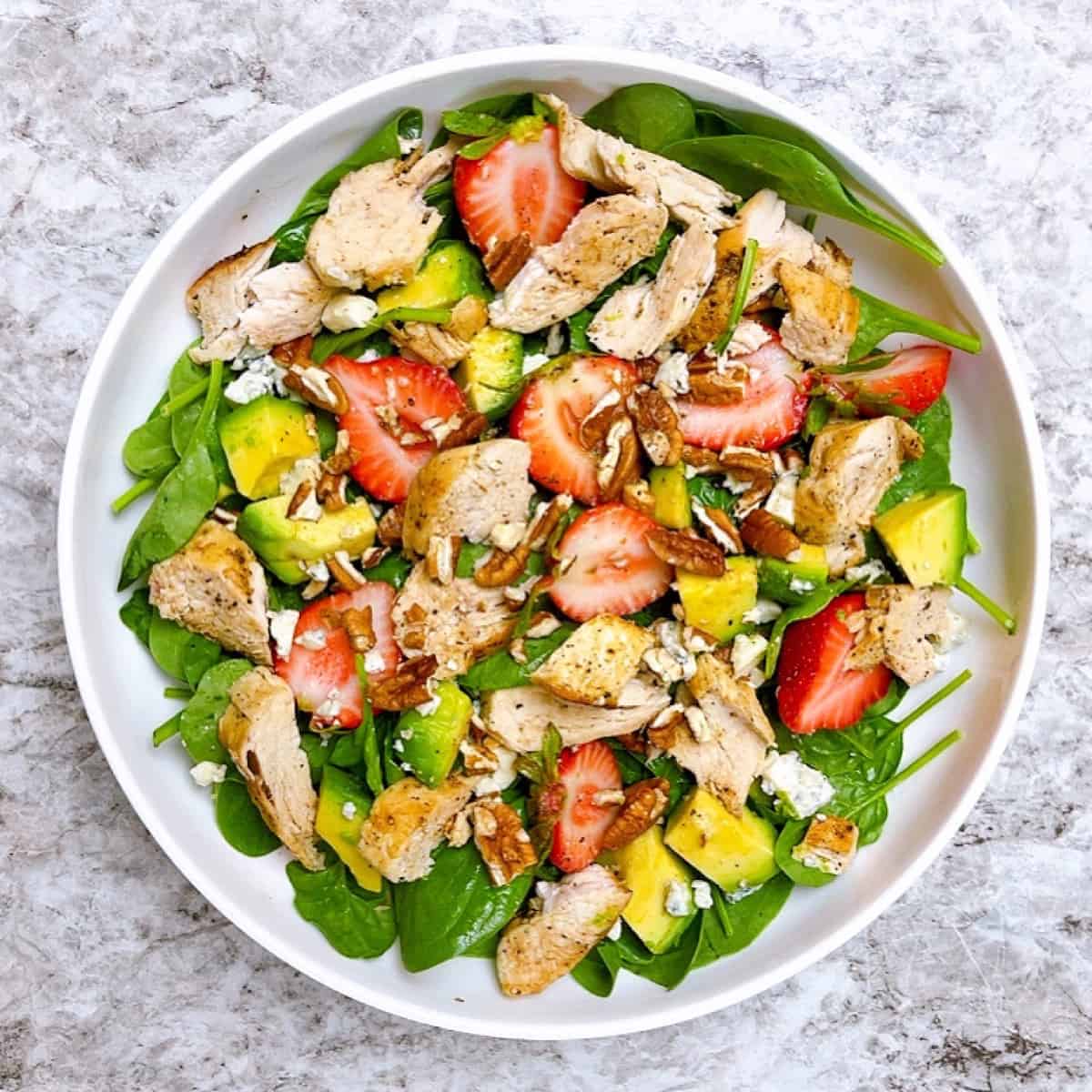 Large white bowl of strawberry spinach salad with avocado and pecans