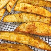 Cooked air fryer potato wedges on air fryer tray with seasoning.