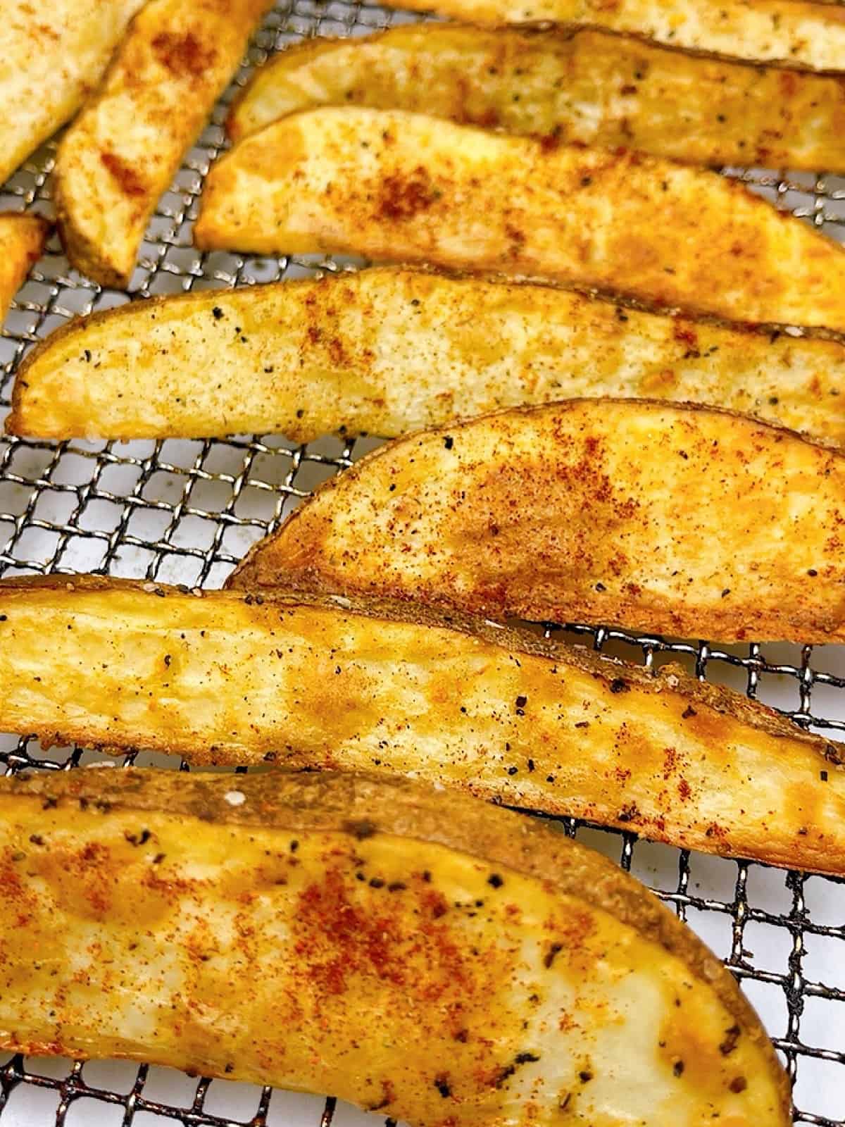 Close up of potato wedges with seasoning on air fryer tray.