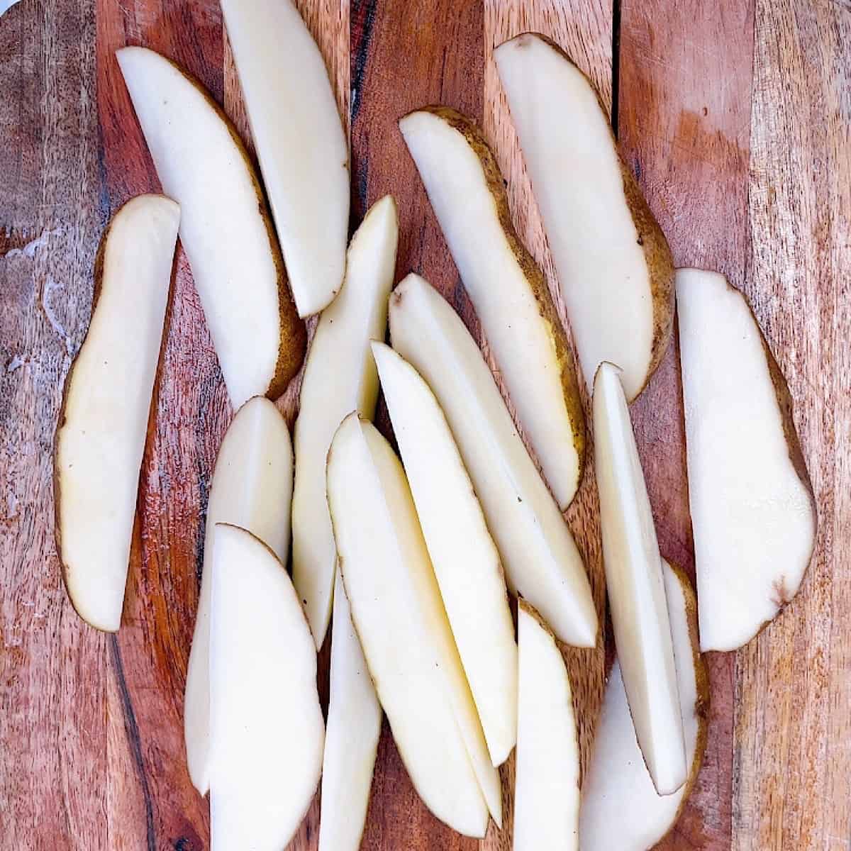 Raw potatoes cut on a wooden cutting board.