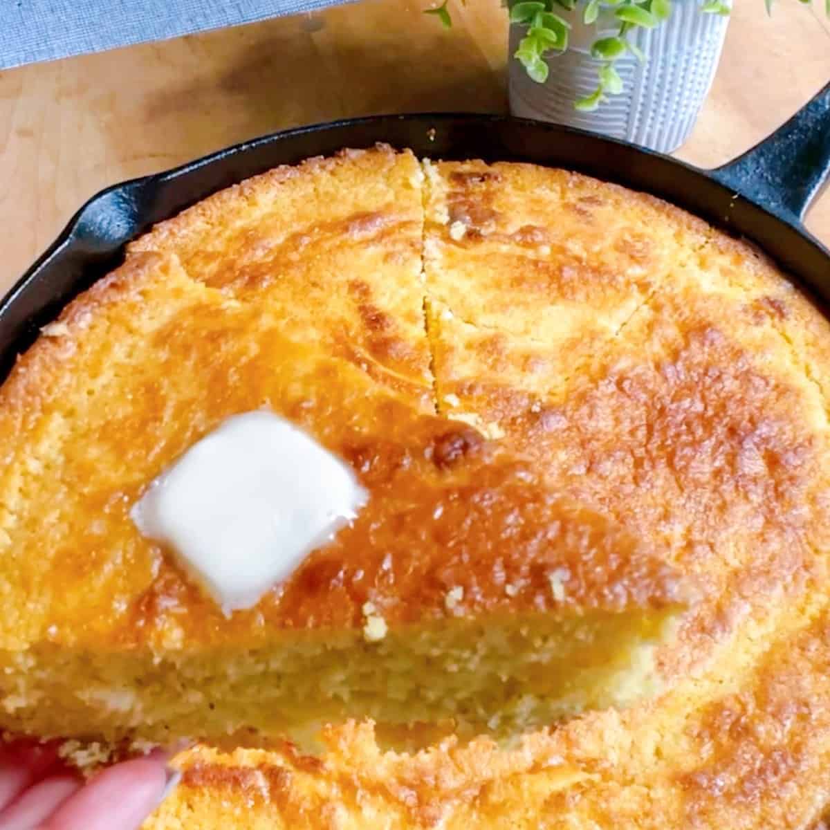 Crispy cornbread sliced in a cast iron skillet with a pat of butter.