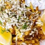 Crispy Greek Fries with lemon feta and dill on a plate with tzatziki sauce.