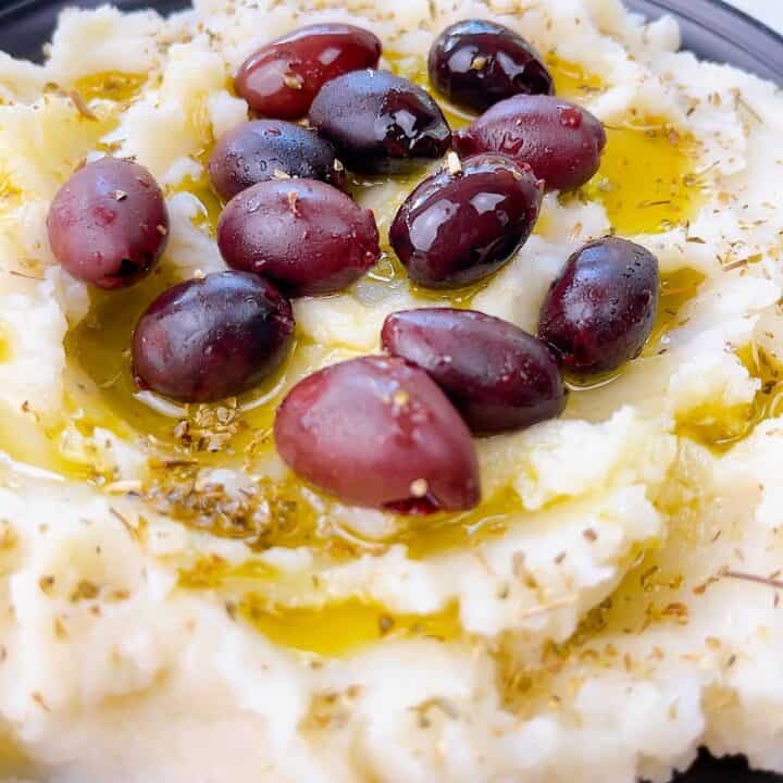 Skordalia dip close up with olives, oil, and herbs on top