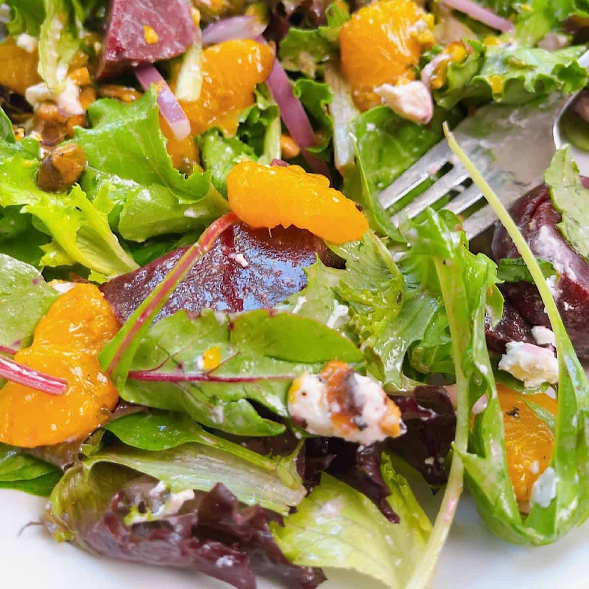 The BEST mandarin orange salad recipe {with Beets} feature image. Close up of tossed salad with fork