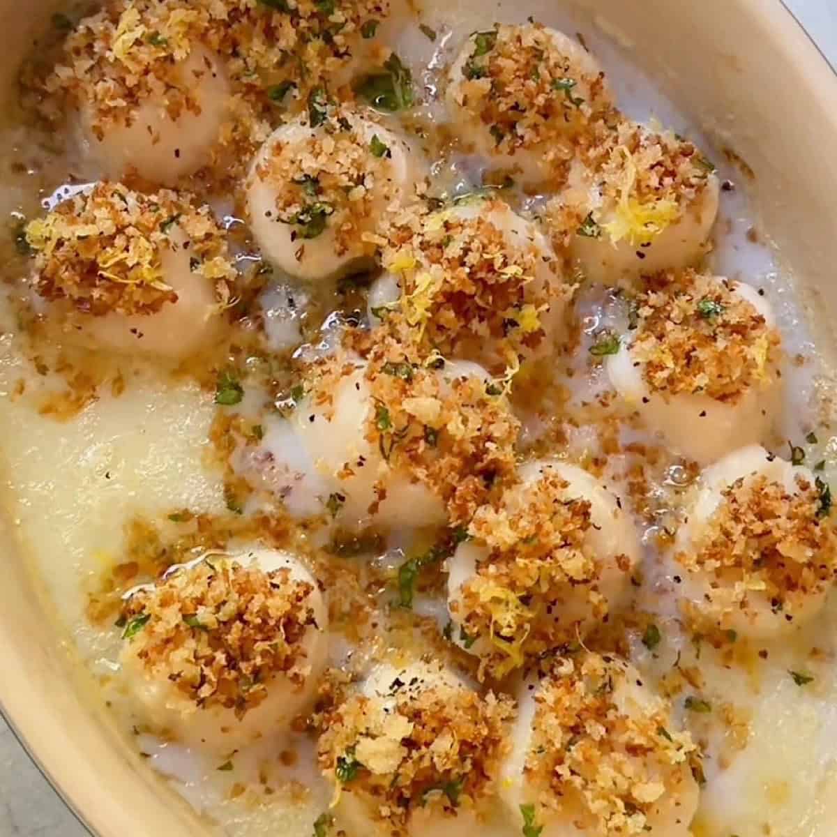 Baked sea scallops with panko parsley and lemon zest topping in baking dish.
