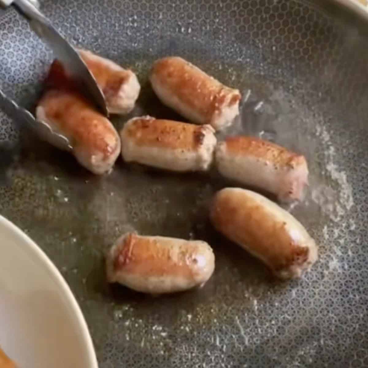 Searing Italian sausages in a skillet with oil.