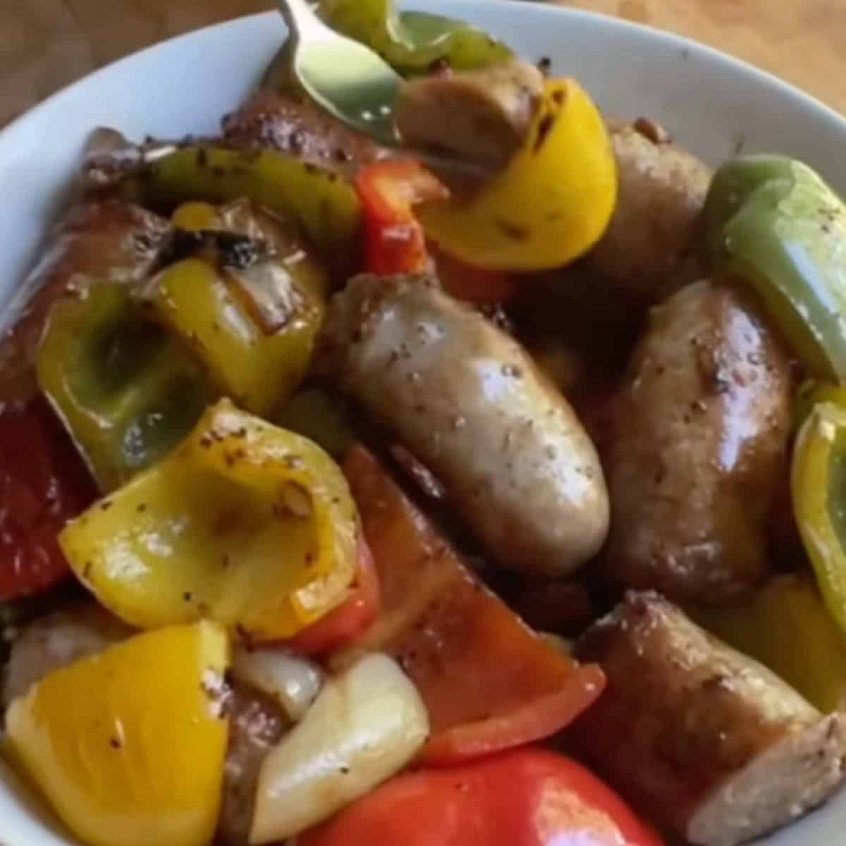 Prepared Italian Sausage and Peppers in white wine sauce in a serving bowl with fork holding a bite sized portion.