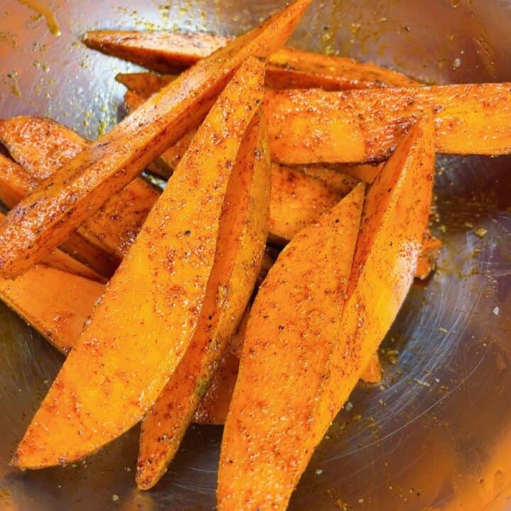 air fryer sweet potato wedges in mixing bowl with seasonings added