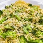 broccoli orzo in white bowl with lemon wedge and parmesan on top.