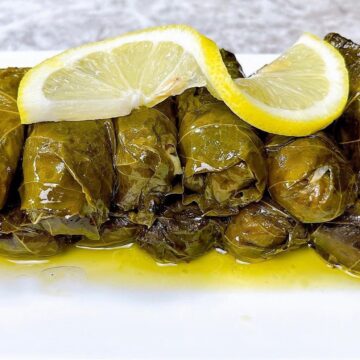 Dolmades on a platter with lemon sauce and a lemon on top.
