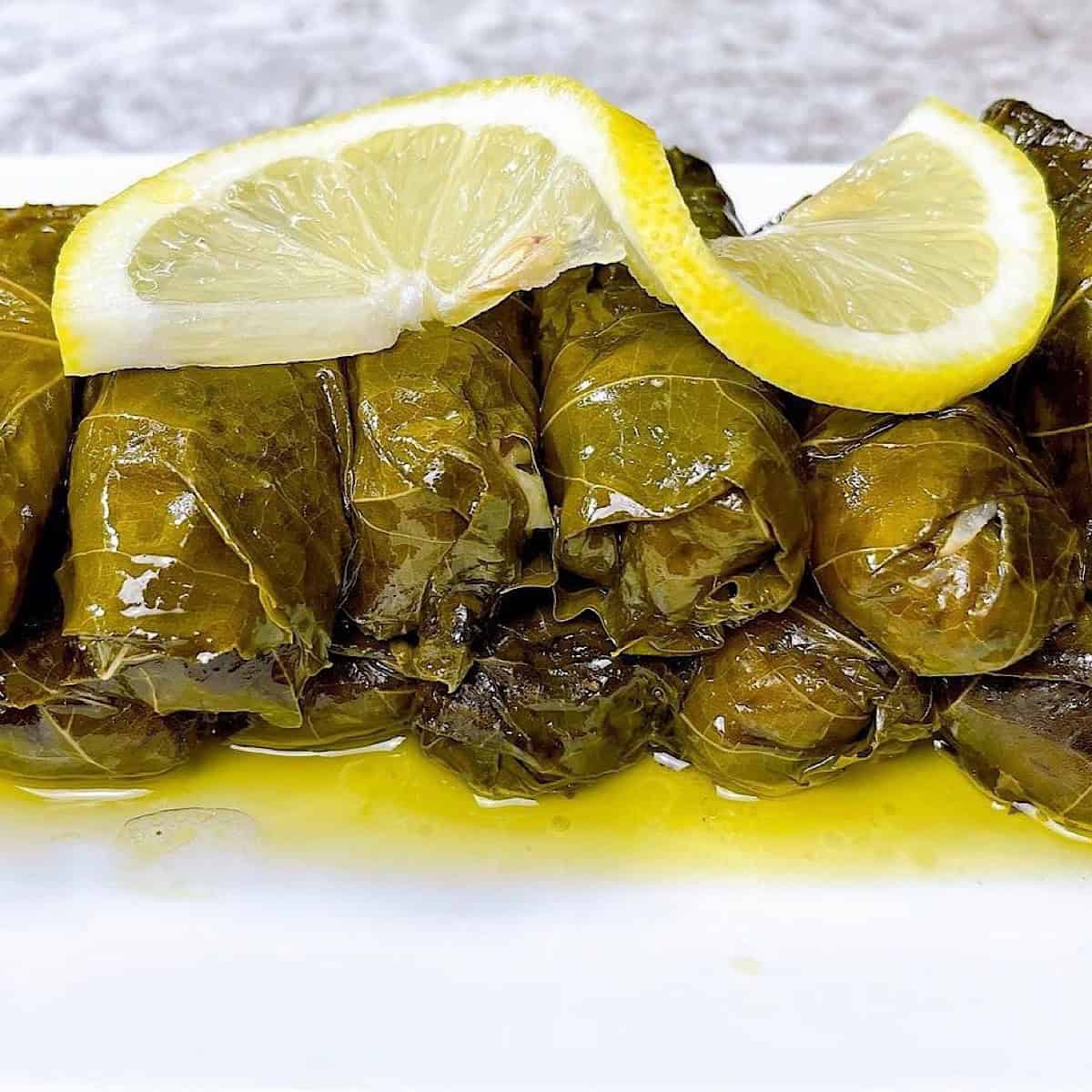 Dolmades on a platter with lemon sauce and a lemon on top.