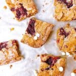A feature image of raspberry blondie squares on parchment paper with white chocolate chips scattered around.