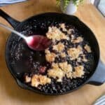 Old fashioned blueberry cobbler feature image in skillet with spoon.