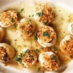 Panko crusted scallops in baking dish with butter and topped with parsley